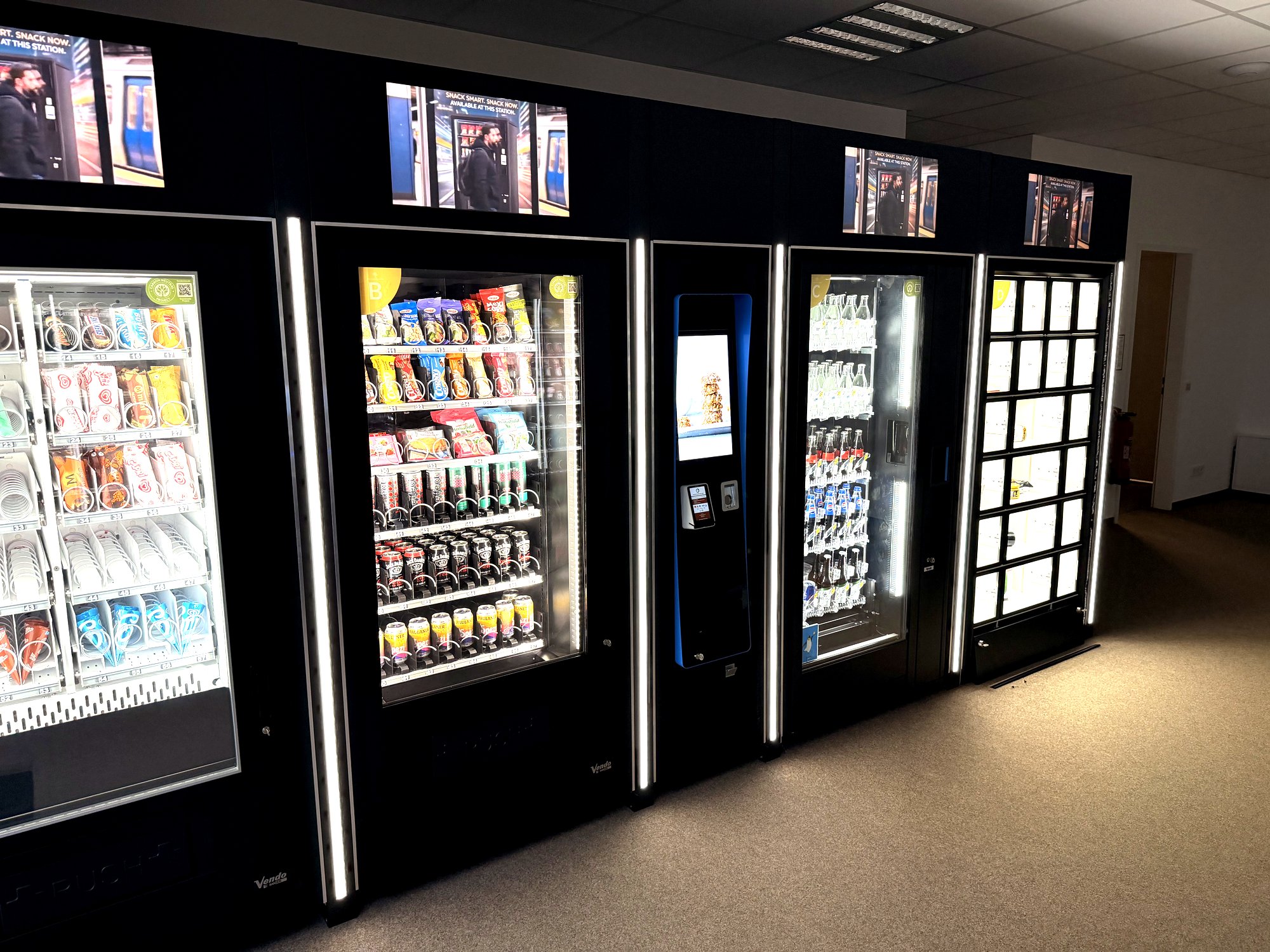 Automatenstore mit beleuchteten Snack-, Getränke- und Schließfachmodulen und leuchtenden Werbetoppern